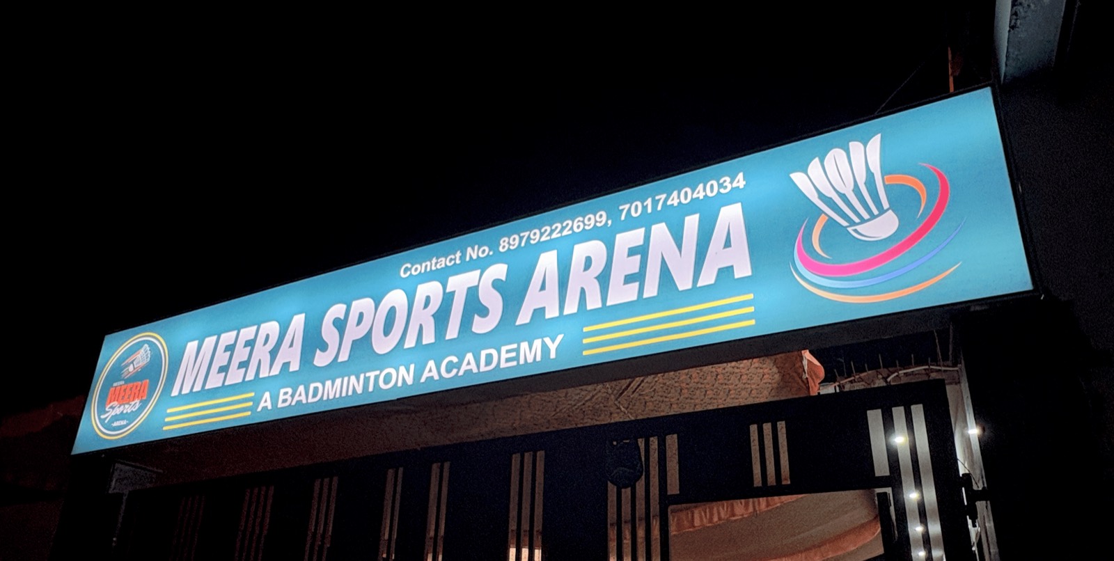 The lit Meera Sports Arena signboard at the entrance gate